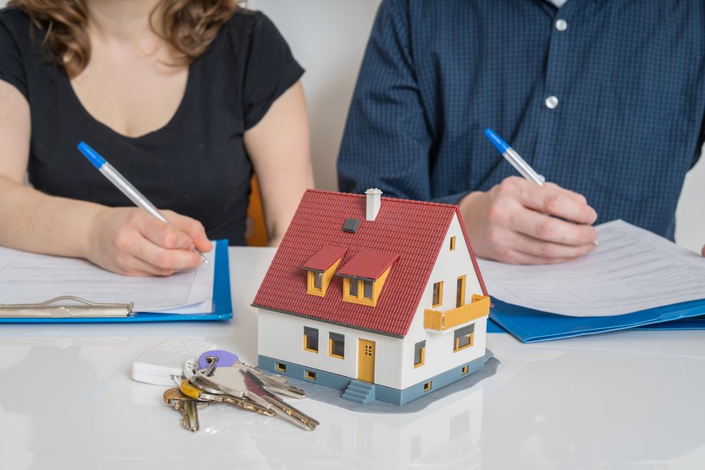 A man and a woman with pen and paper, a model house and keys in front of them, representing division of property